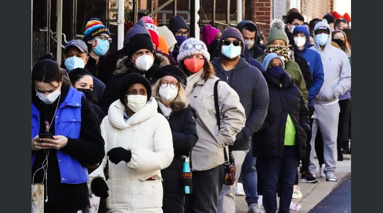 Decenas de residentes de la ciudad hacen una fila que se extiende alrededor de la cuadra para recibir kits gratuitos de prueba rápida de COVID-19 en el hogar, el lunes 20 de diciembre de 2021 en Filadelfia. (AP Foto/Matt Rourke)