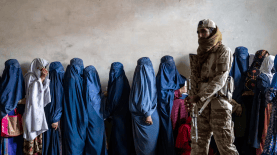 Un combatiente talibán monta guardia mientras unas mujeres esperan para recibir raciones de comida distribuidas por un grupo de ayuda humanitaria, en Kabul, Afganistán, en mayo de 2023. (AP Photo/Ebrahim Noroozi, File)